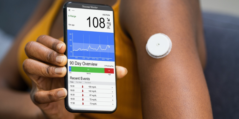 Close-up of a continuous glucose monitor on a woman's arm, displaying real-time blood sugar data on a smartphone.