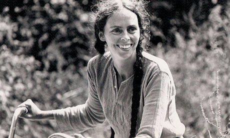 Young Ina May Gaskin, founder of modern midwifery, smiling while riding a bicycle at The Farm in Tennessee.