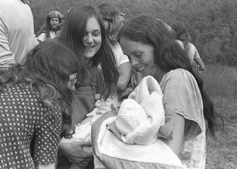 Young Ina May Gaskin holding a newborn baby at The Farm, surrounded by women during a natural birth gathering.