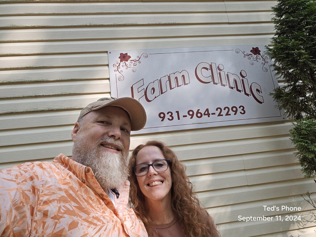 Jaelin and Ted Stickels at The Farm Midwifery Center in Summertown, Tennessee, standing in front of the Farm Clinic sign.