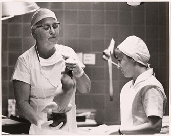 Dr. Virginia Apgar holding a newborn in a hospital delivery room while assessing the baby’s health.