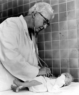 Dr. Virginia Apgar using a stethoscope to examine a newborn in a hospital setting.