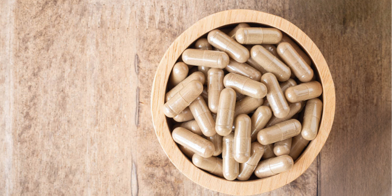 Encapsulated placenta pills in a wooden bowl on a rustic wooden surface.