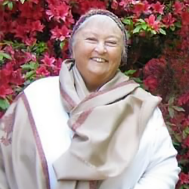 Sister Angela Murdaugh smiling in front of blooming red flowers, wearing a shawl